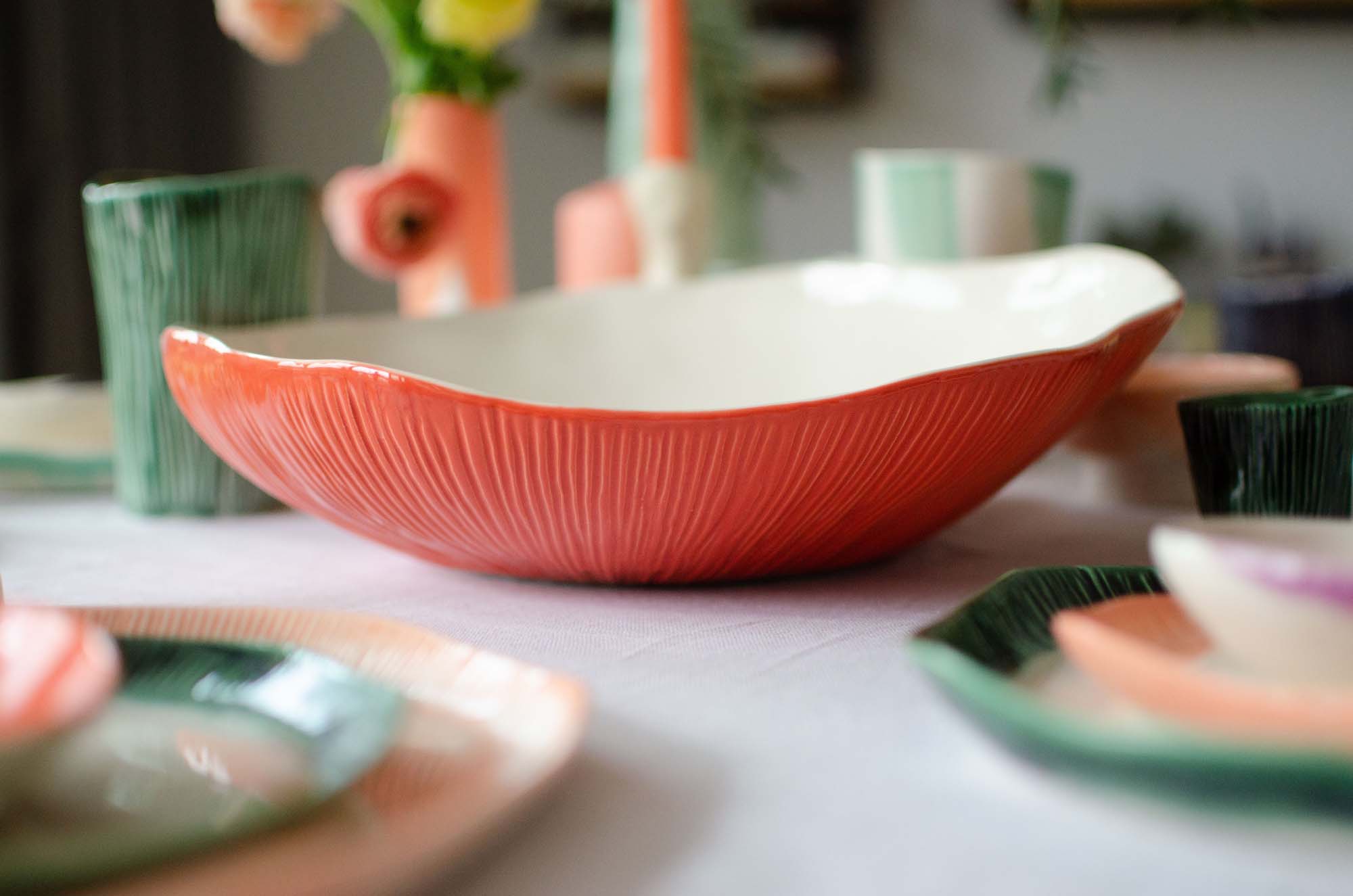 Close-up of a large handmade porcelain bowl with red textured exterior and white interior, surrounded by matching colorful ceramic tableware.