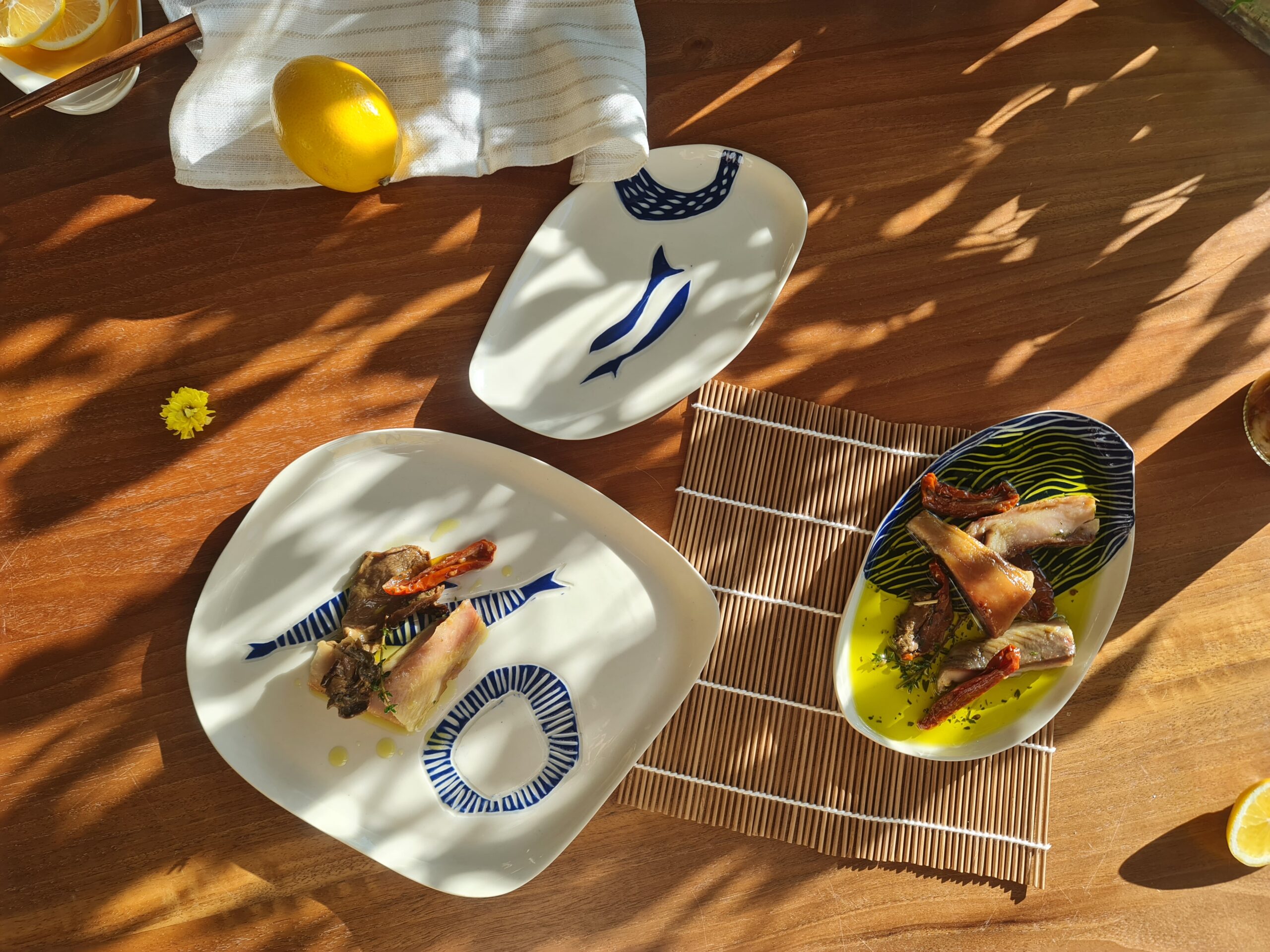 Porcelain fish plates with blue sgraffito designs, served with seafood dishes on a sunlit wooden table.