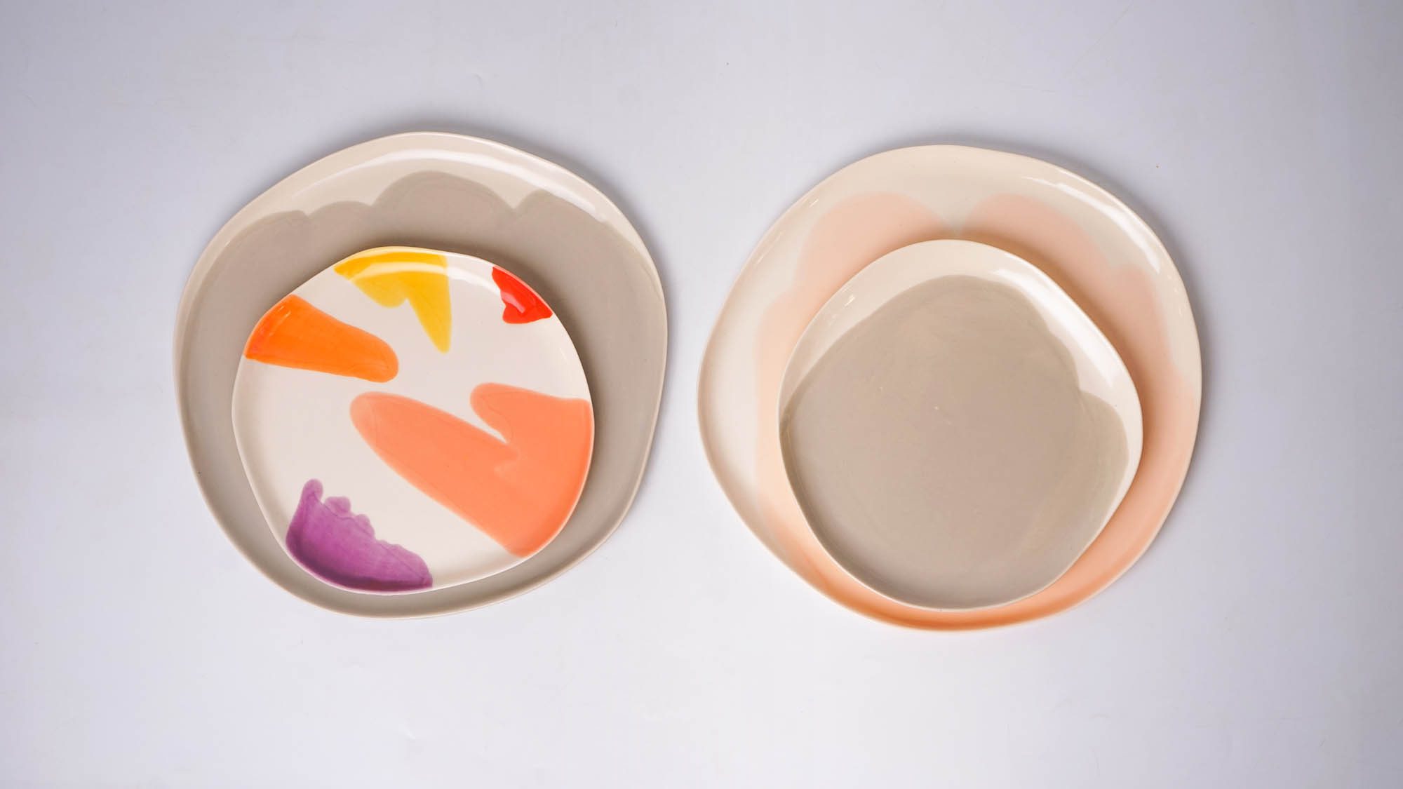 Two sets of layered porcelain plates — one with multicolored brushstrokes, the other in soft neutral tones.