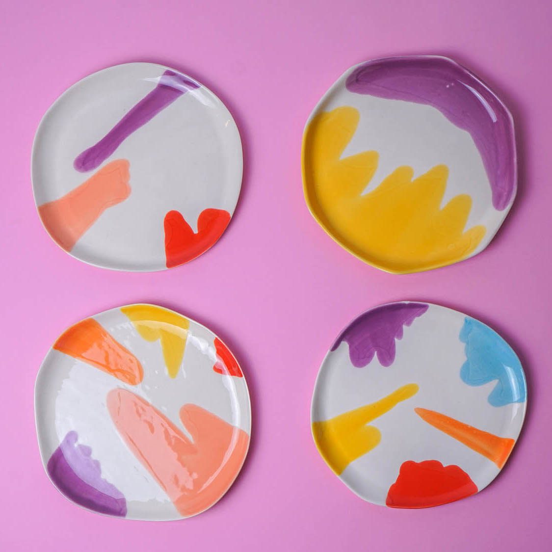 Four colorful porcelain plates with abstract brushstrokes on a pink background.