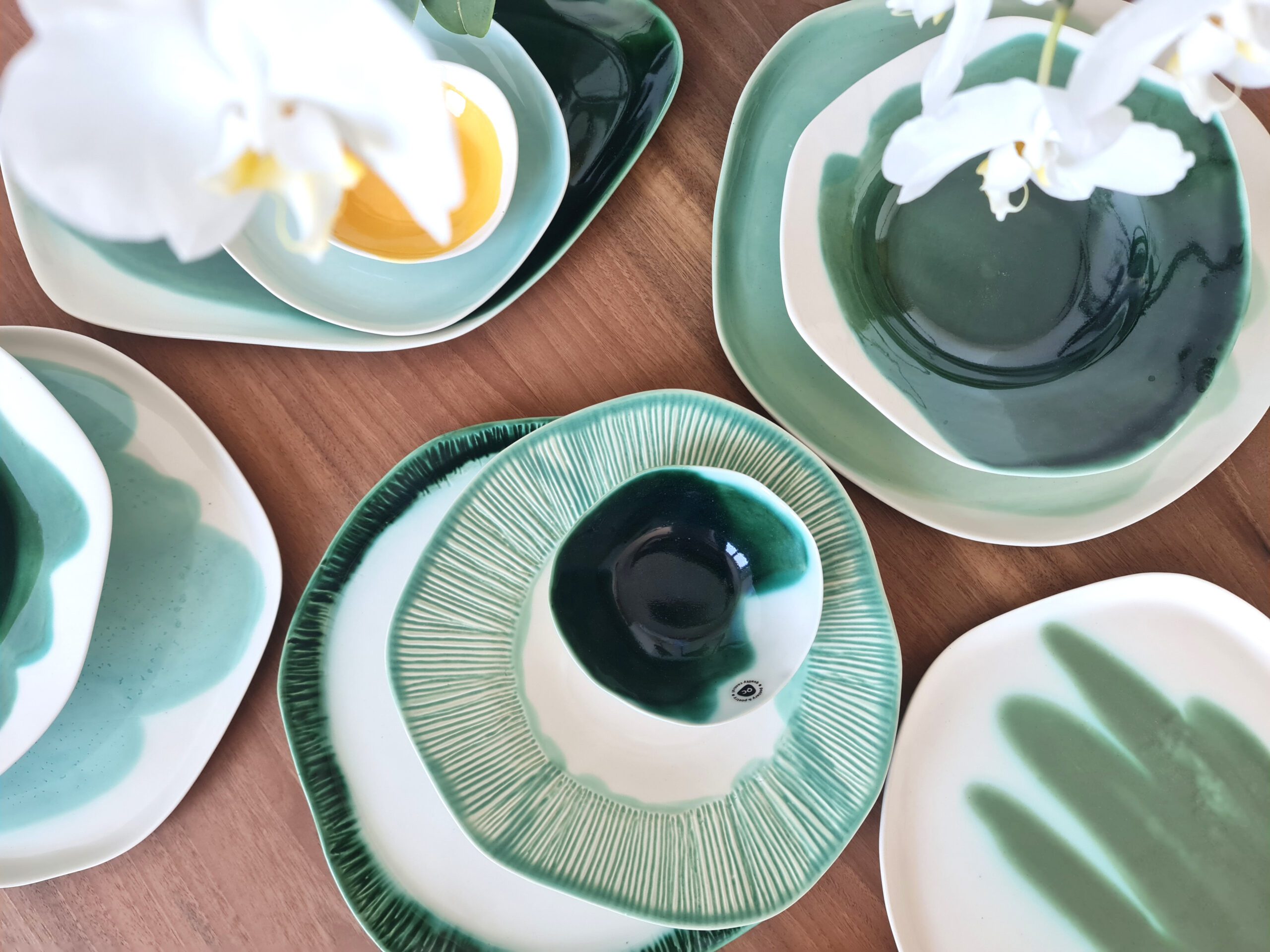 Top view of a spring-inspired table setting with handmade porcelain plates and bowls in soft and deep greens, featuring both smooth and textured designs.
